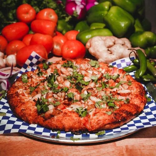 Clickable image showing A pizza with toppings of tomato, onions and cilantro that's been baked to perfection. Should open an Instagram external link to the source image.